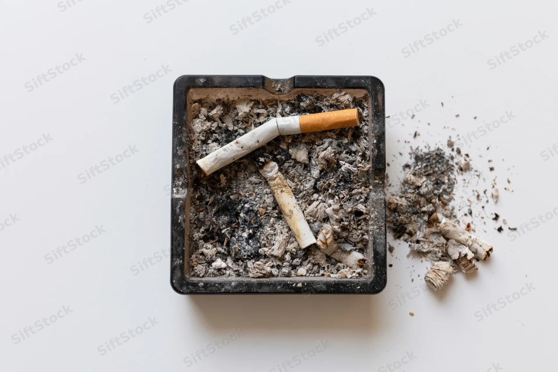 Dirty black square glass ashtray filled with cigarette ash and butts on white background