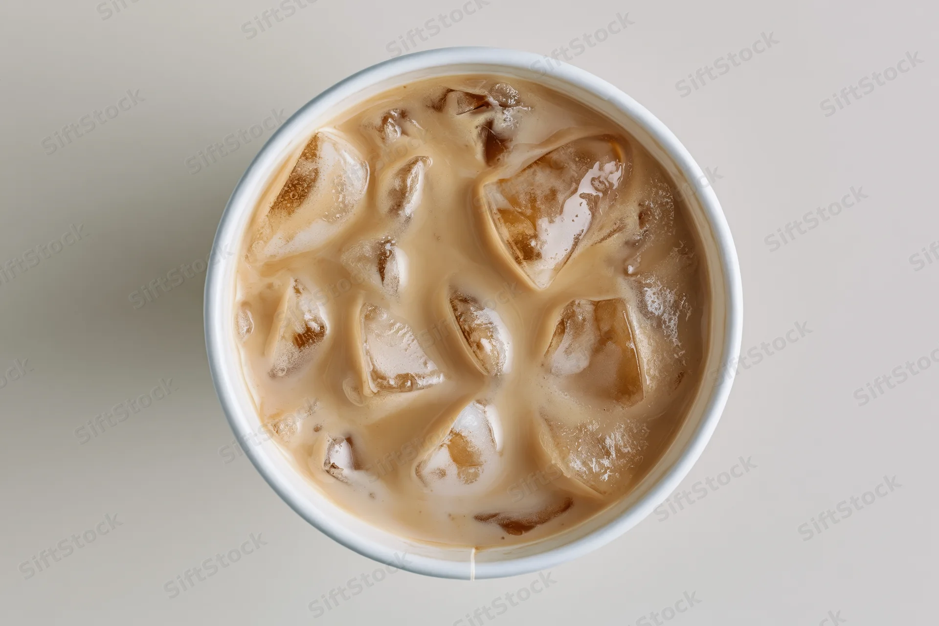 Iced latte in a white paper cup viewed from above with ice cubes and creamy swirls