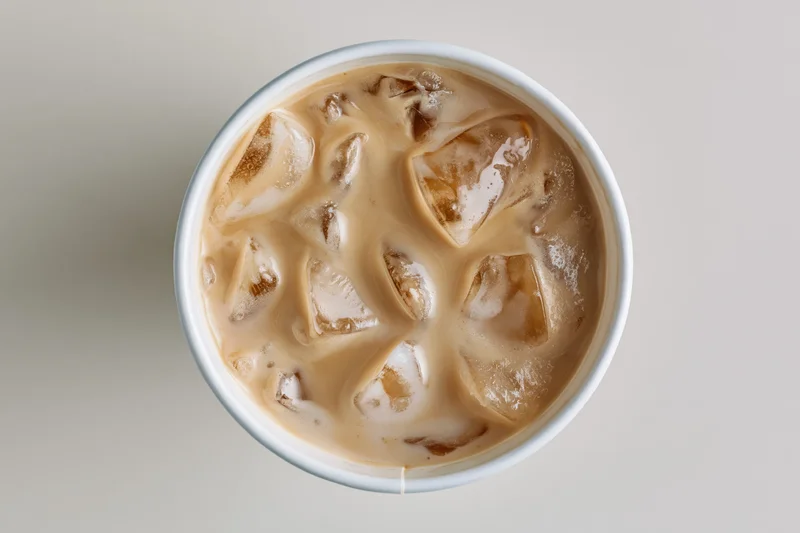 Iced latte in a white paper cup viewed from above with ice cubes and creamy swirls