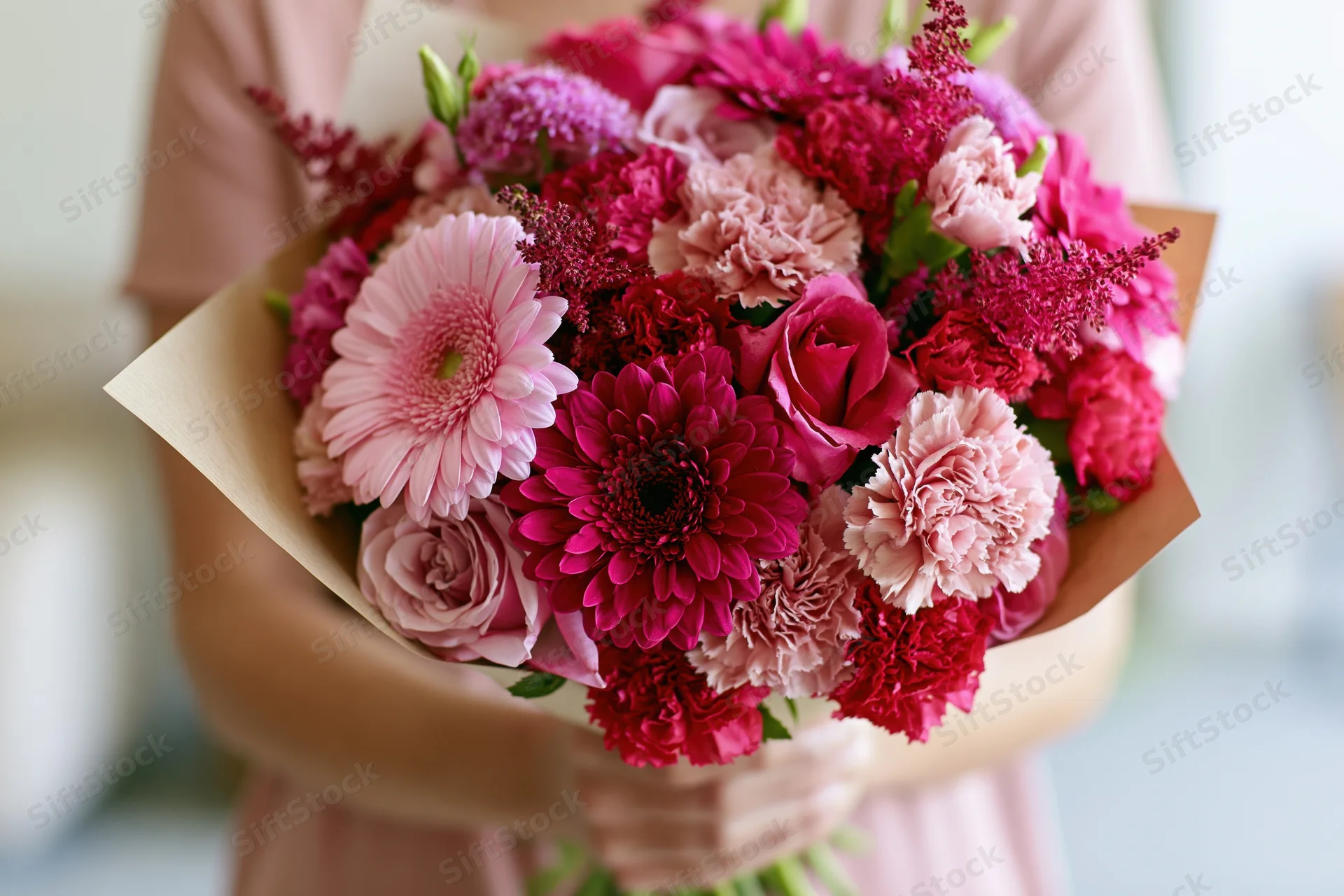 Woman holding a mixed pink and red floral bouquet wrapped in kraft paper