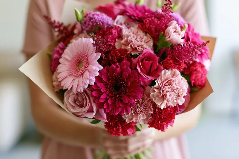 Woman holding a mixed pink and red floral bouquet wrapped in kraft paper