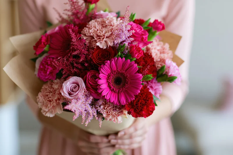 Woman holding a mixed pink and red floral bouquet wrapped in kraft paper