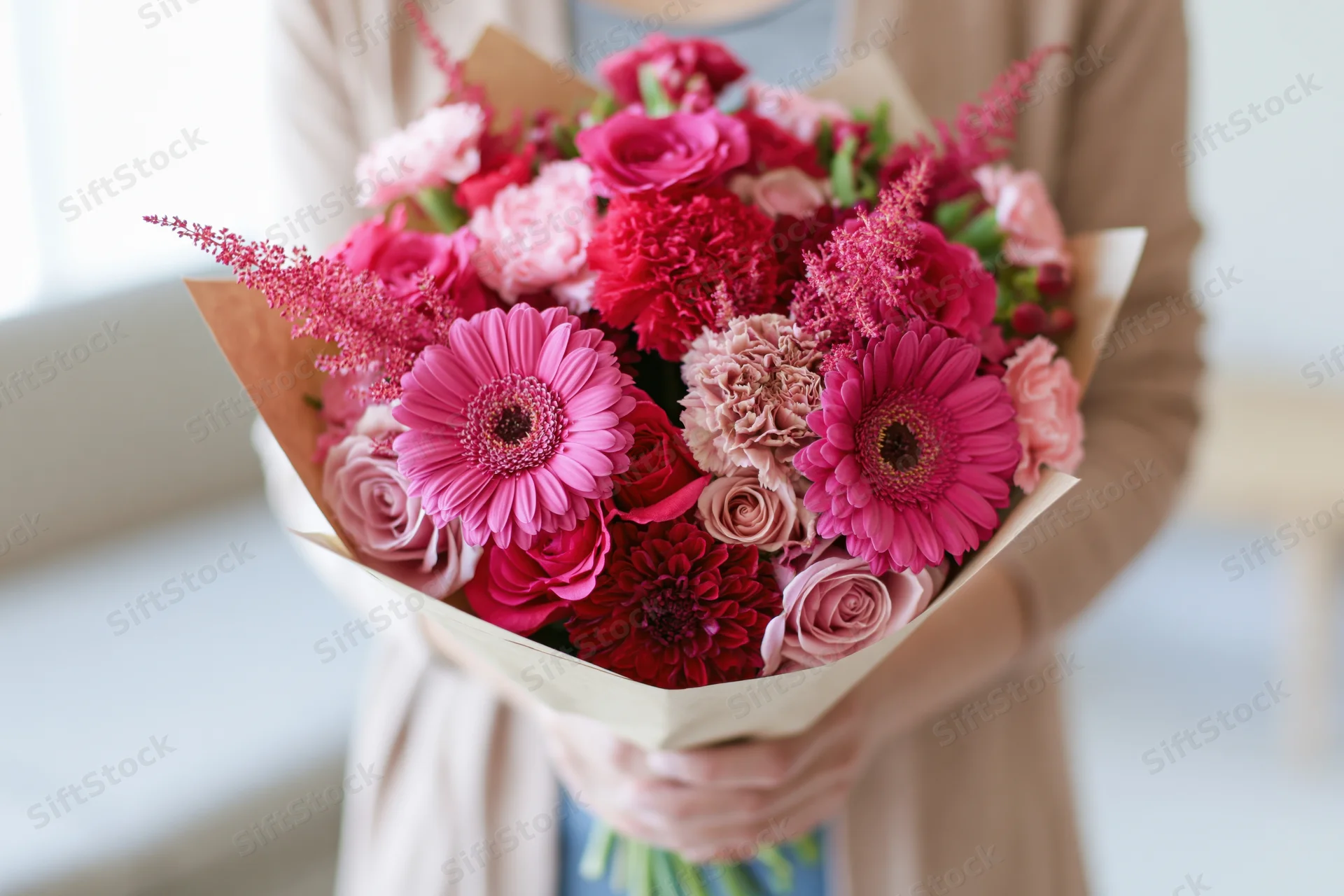 Woman holding a mixed pink flower bouquet wrapped in kraft paper