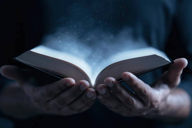 Hands holding open hardcover book with glowing light and floating particles in dark setting