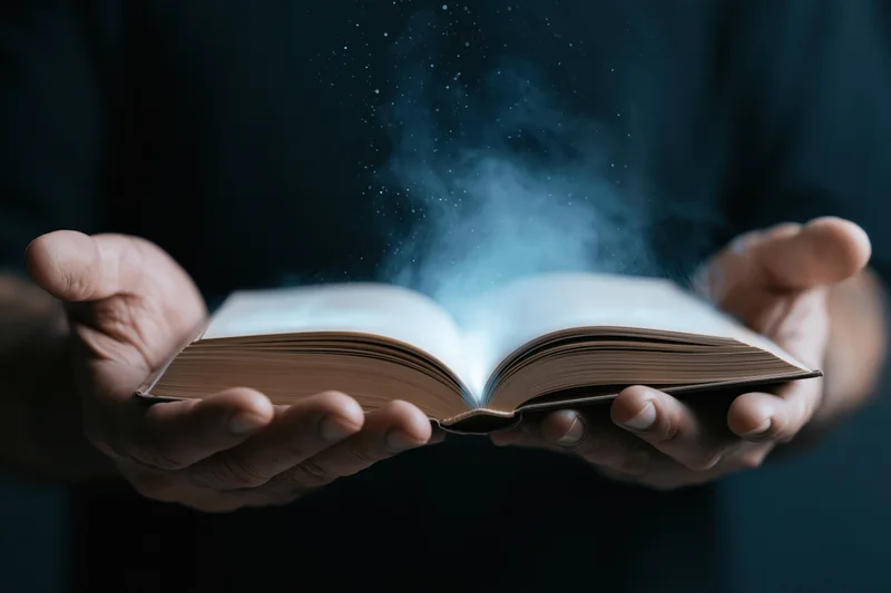Hands holding open hardcover book with glowing blue particles rising from pages