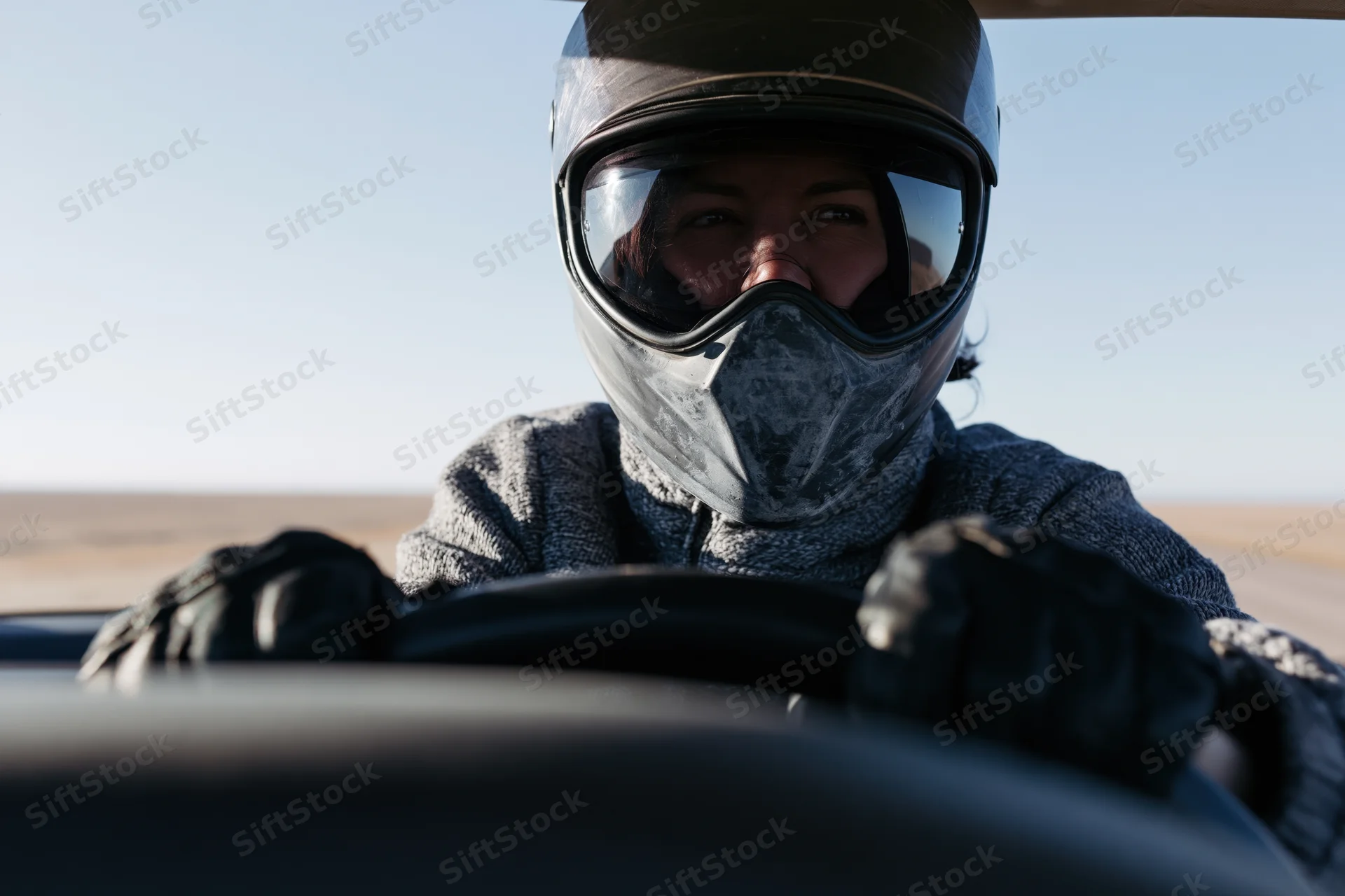Woman in motorcycle helmet gripping steering wheel while riding on open desert road