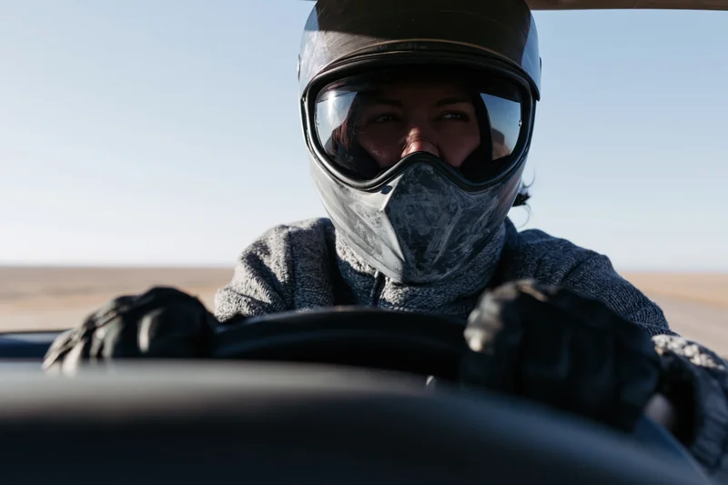Woman in motorcycle helmet gripping steering wheel while riding on open desert road