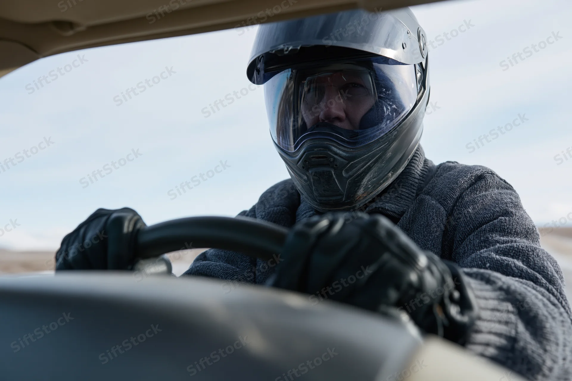 Man in full-face motorcycle helmet gripping steering wheel while driving vehicle in desert landscape