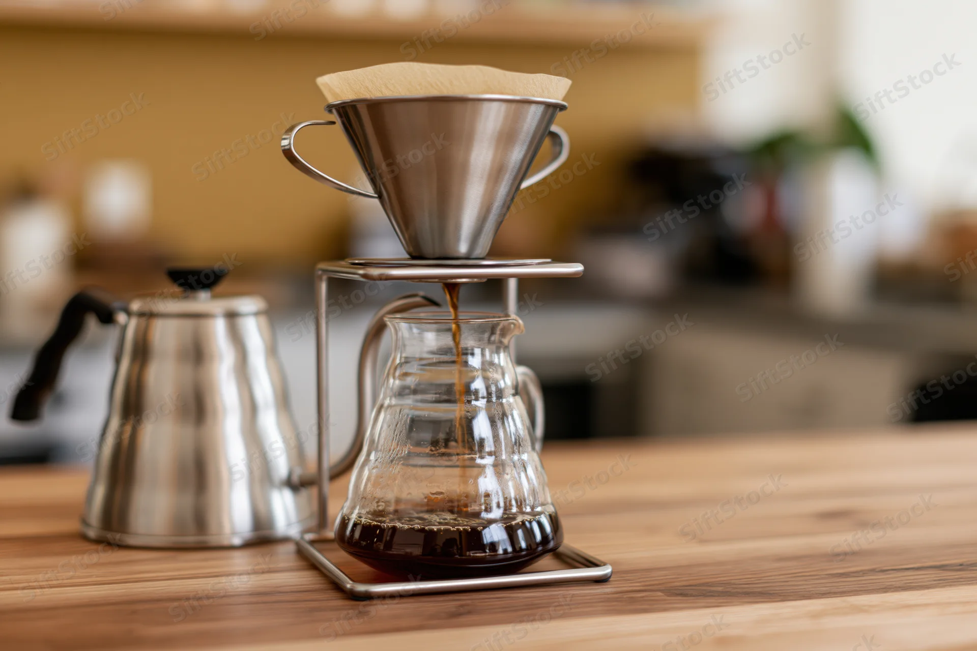 Pour-over coffee brewing setup on wooden counter with glass carafe and metal kettle