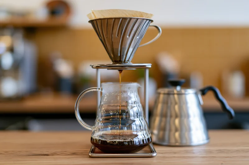 Pour-over coffee brewing setup on wooden cafe counter with glass carafe and metal kettle