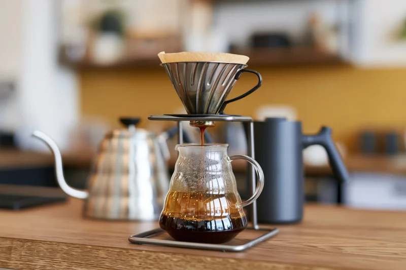 Pour-over coffee brewing setup on wooden counter with glass carafe and metal kettle