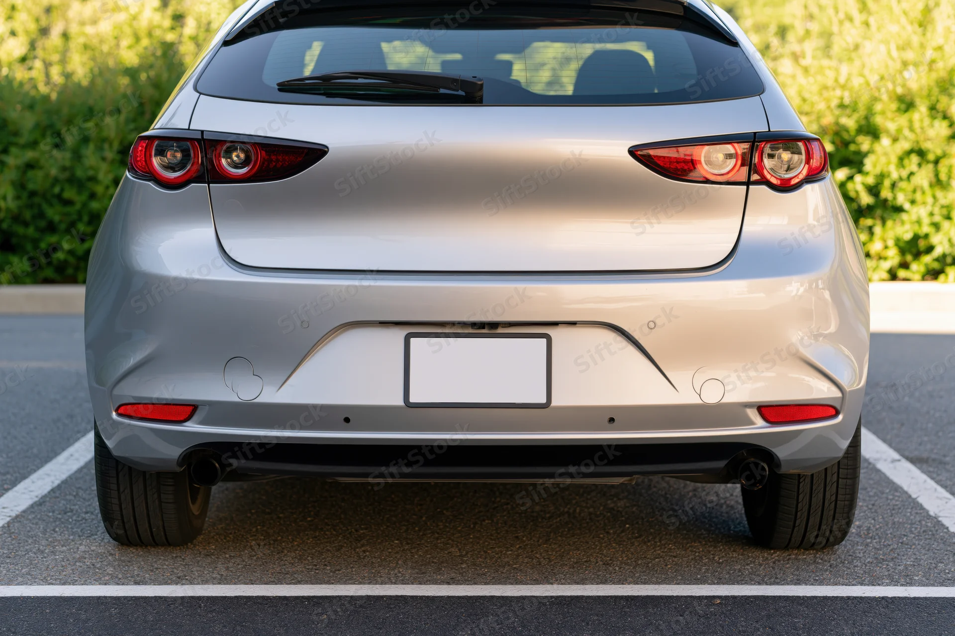 Rear view of a silver compact hatchback parked in an outdoor lot with green foliage in the background