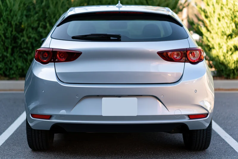 Rear view of a silver compact hatchback parked in an outdoor lot with green foliage in the background