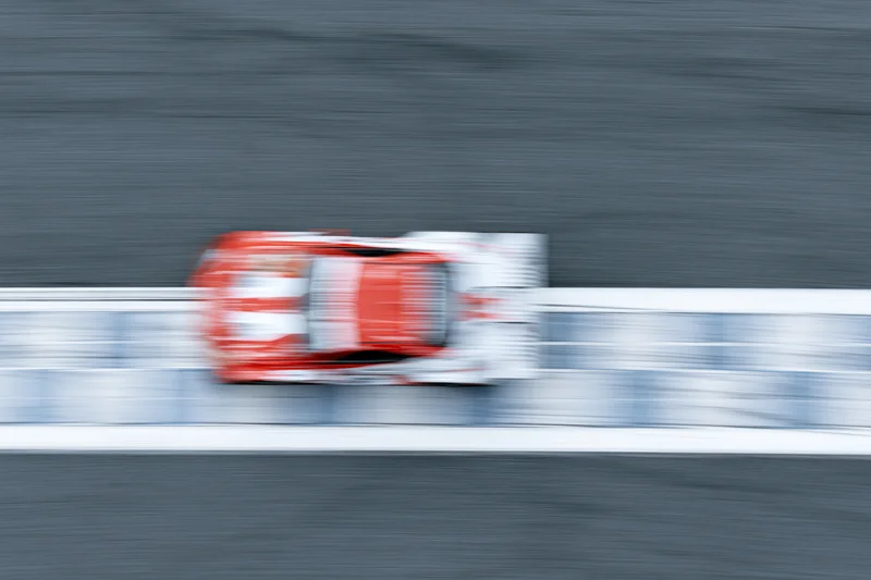 Red and white gt racing car crossing painted finish line on racetrack at high speed
