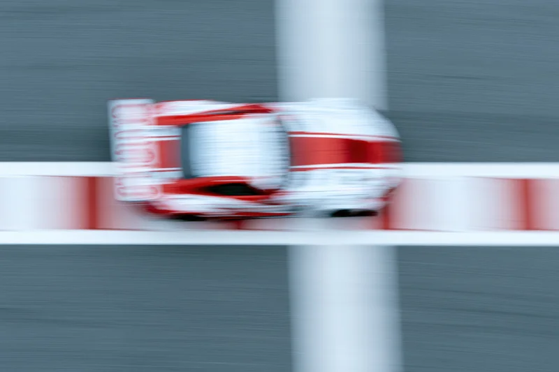 Red and white gt racing car speeding across painted finish line on racetrack