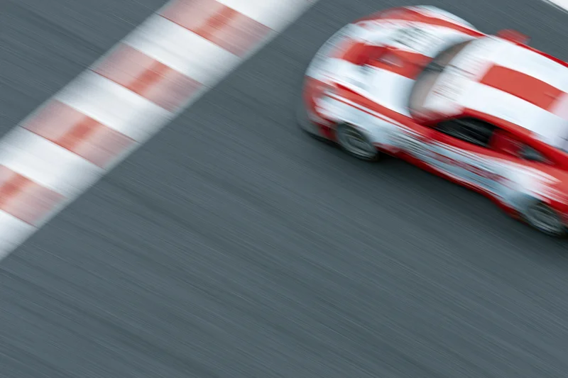 Red and white gt racing car speeding across painted finish line on asphalt track