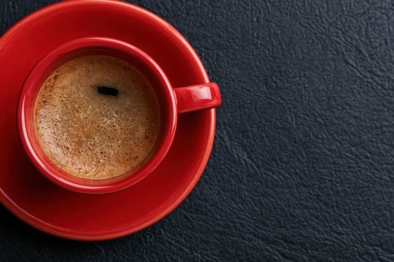 Red ceramic coffee cup filled with espresso and crema on matching saucer on dark textured surface, top view