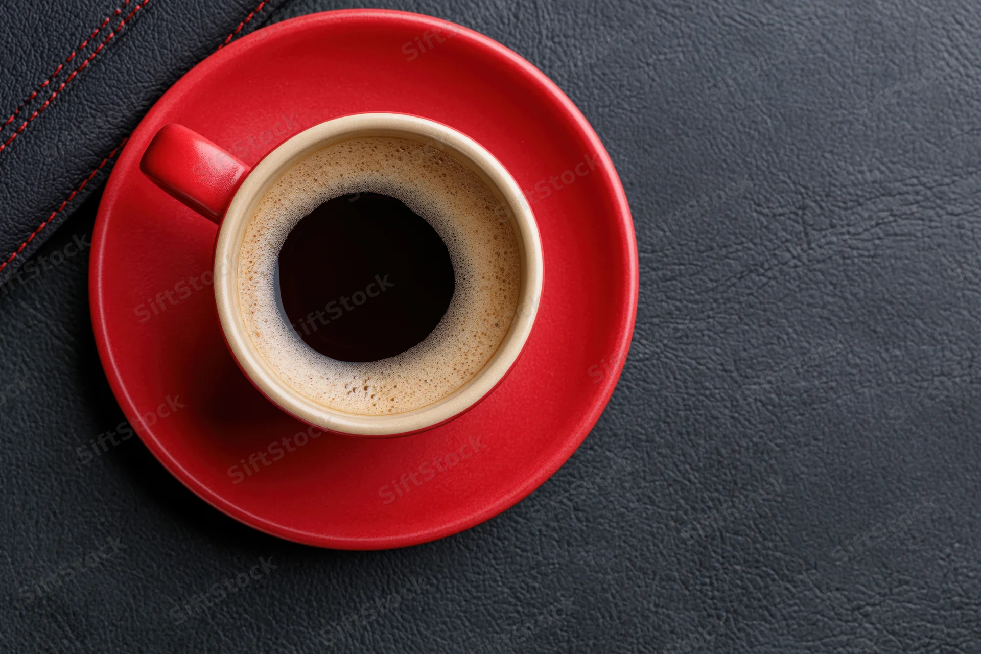 Red ceramic coffee cup with foam on matching saucer on dark leather surface