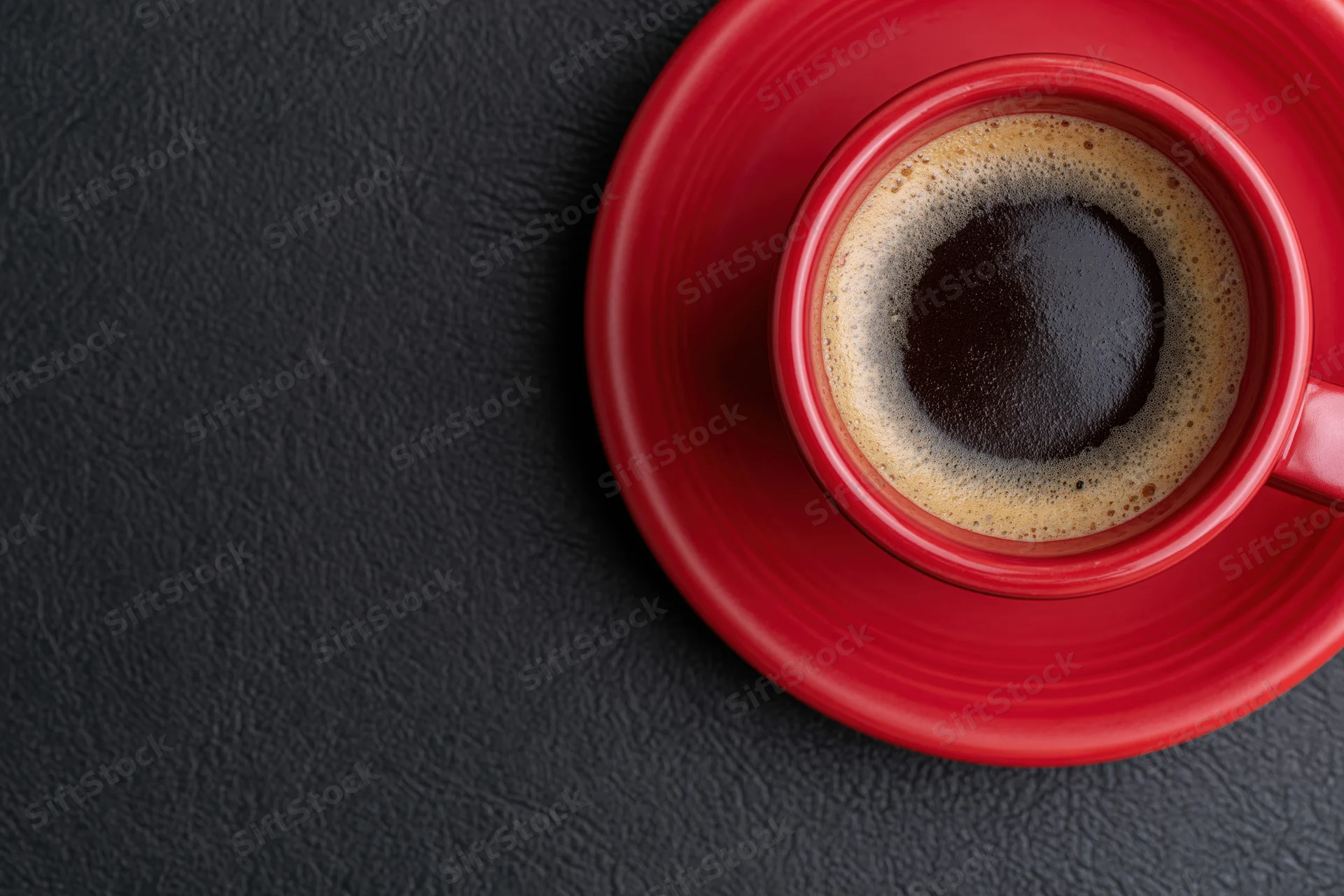 Red ceramic coffee cup filled with espresso on matching saucer on dark textured surface