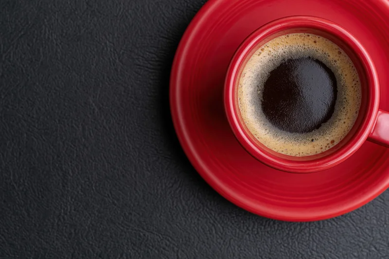 Red ceramic coffee cup filled with espresso on matching saucer on dark textured surface