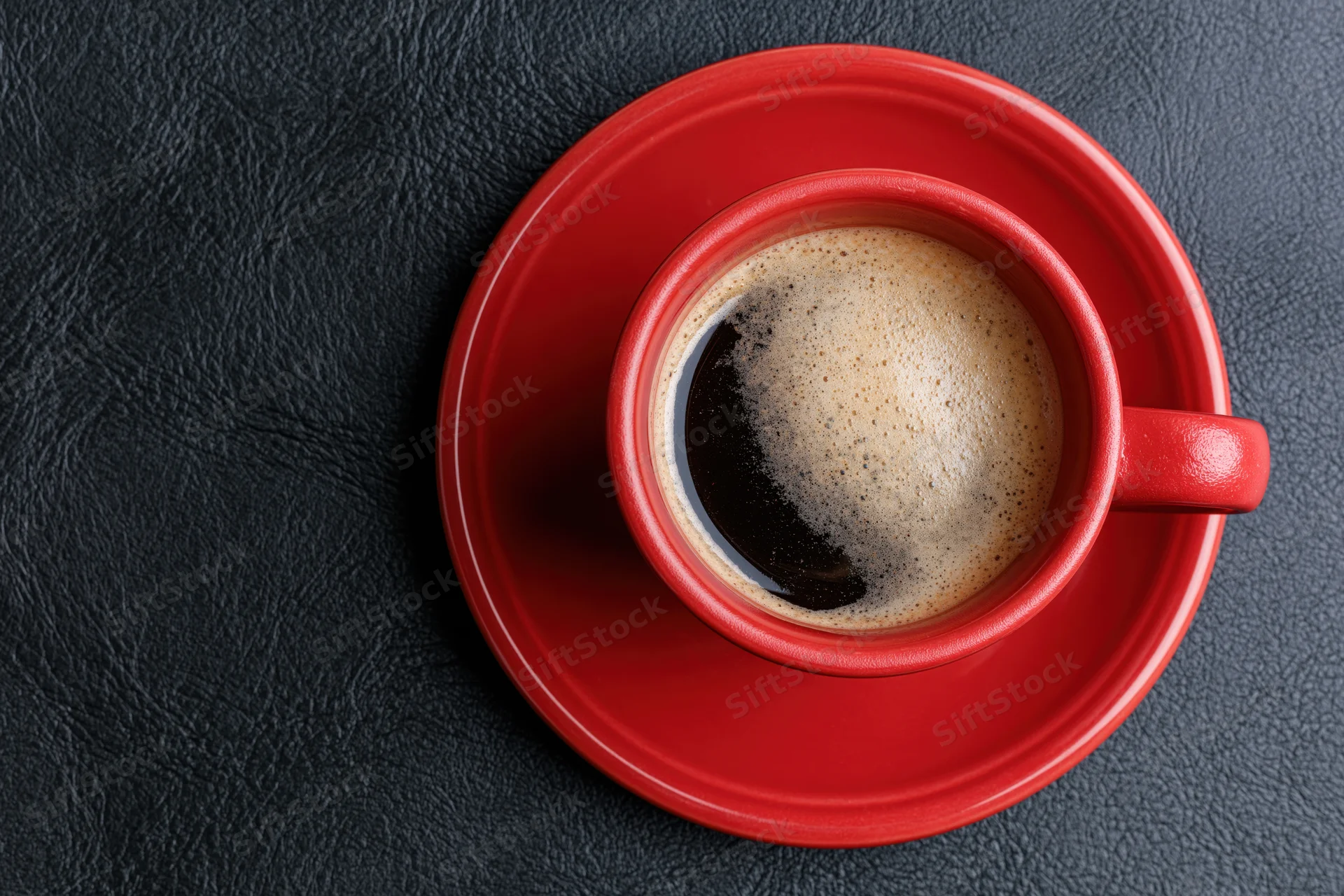 Red ceramic coffee cup filled with espresso and foam on matching saucer on dark textured surface