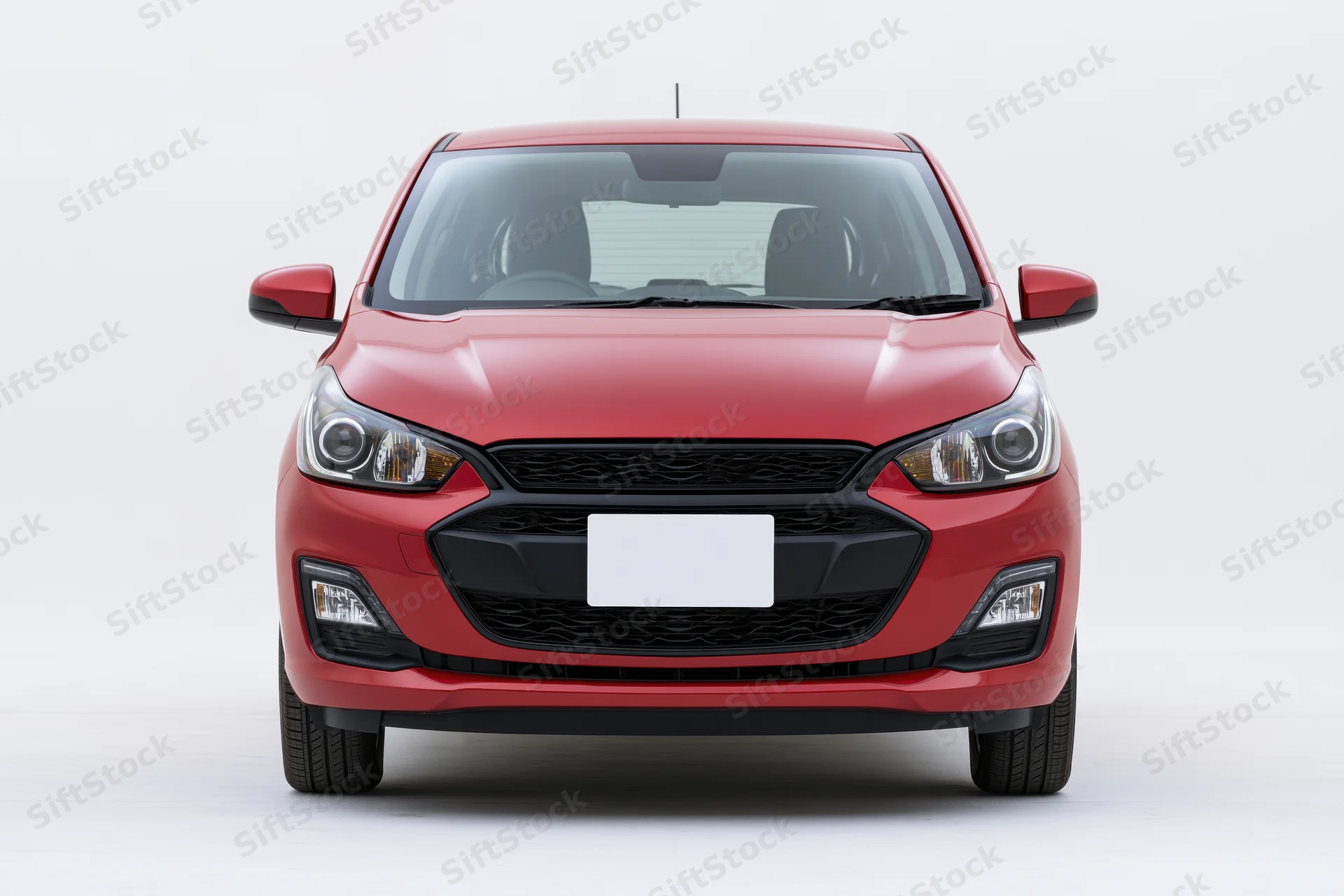 Red compact hatchback car viewed straight-on from front in studio setting