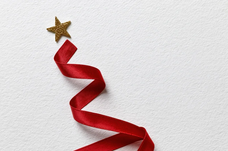 Red satin ribbon arranged in zigzag christmas tree shape with gold star on white background