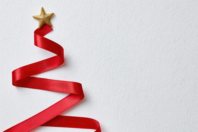 Red satin ribbon arranged in zigzag christmas tree shape on white background with gold star topper