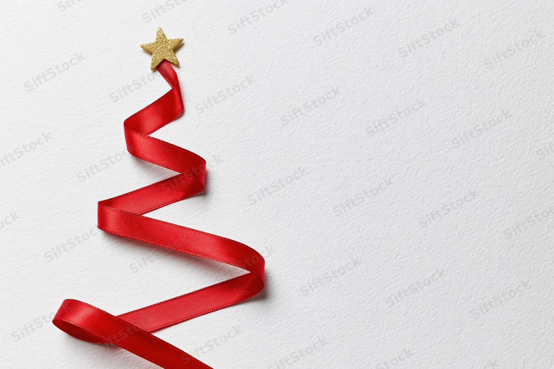 Red satin ribbon arranged in zigzag christmas tree shape on white background with gold star topper