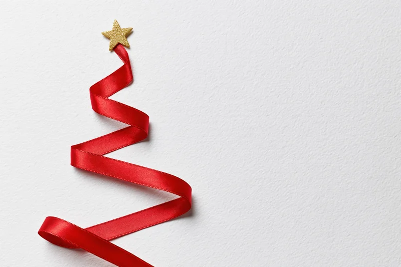 Red satin ribbon arranged in zigzag christmas tree shape on white background with gold star topper