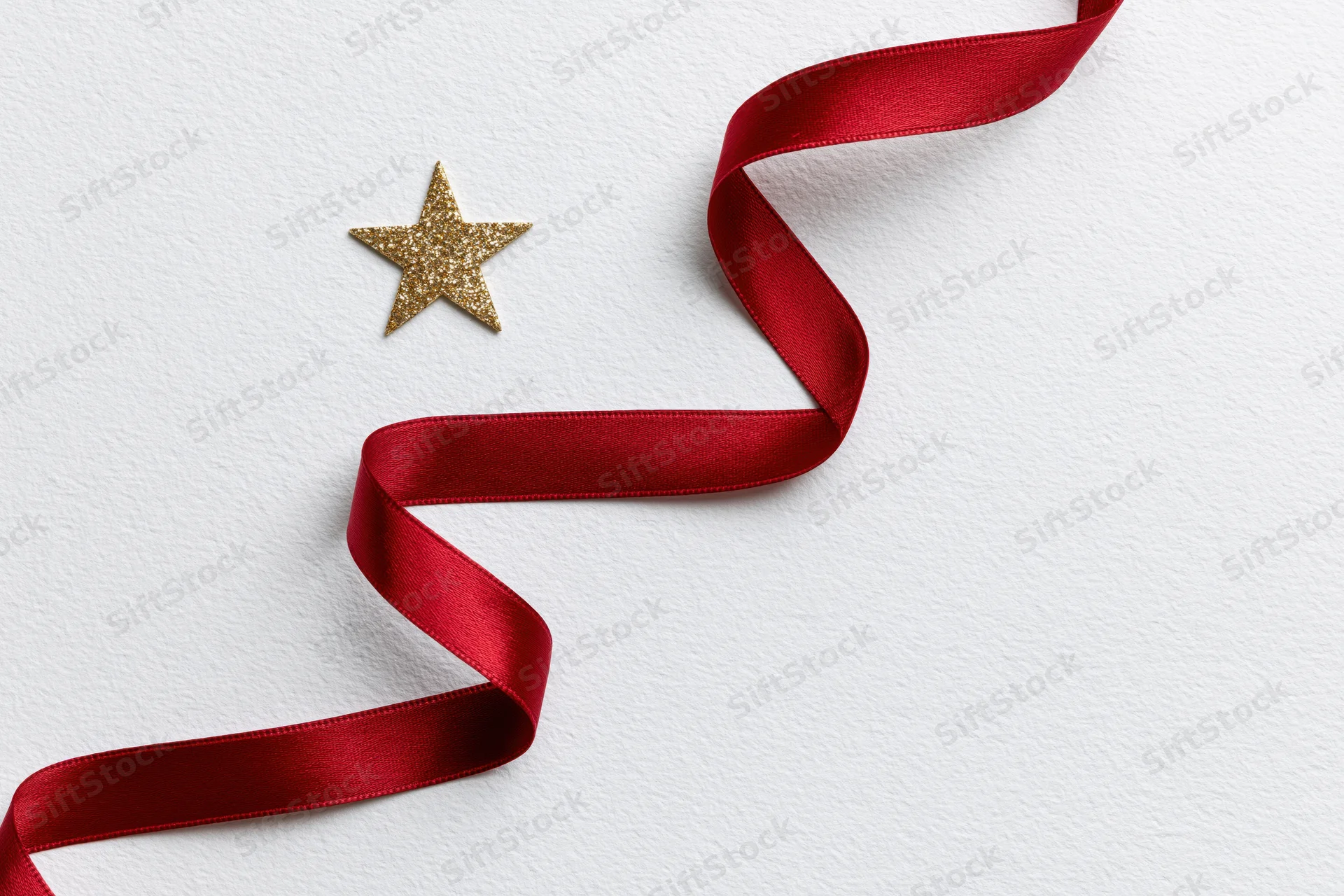Red satin ribbon arranged in zigzag tree shape with gold glitter star on white background