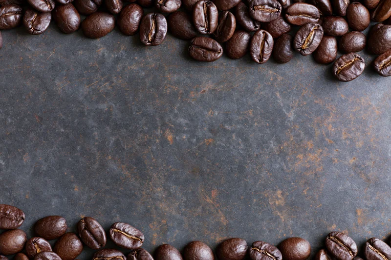 Roasted coffee beans arranged along top and bottom edges on dark textured surface