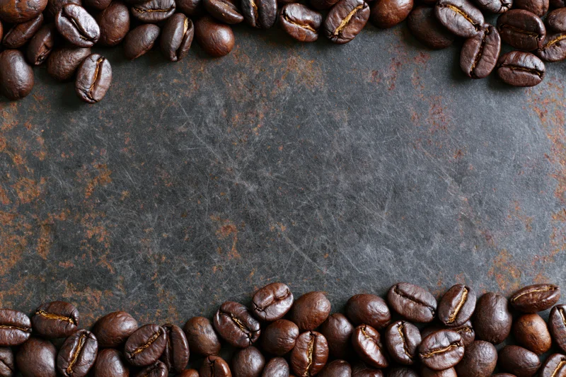 Roasted coffee beans arranged along top and bottom edges on dark textured surface