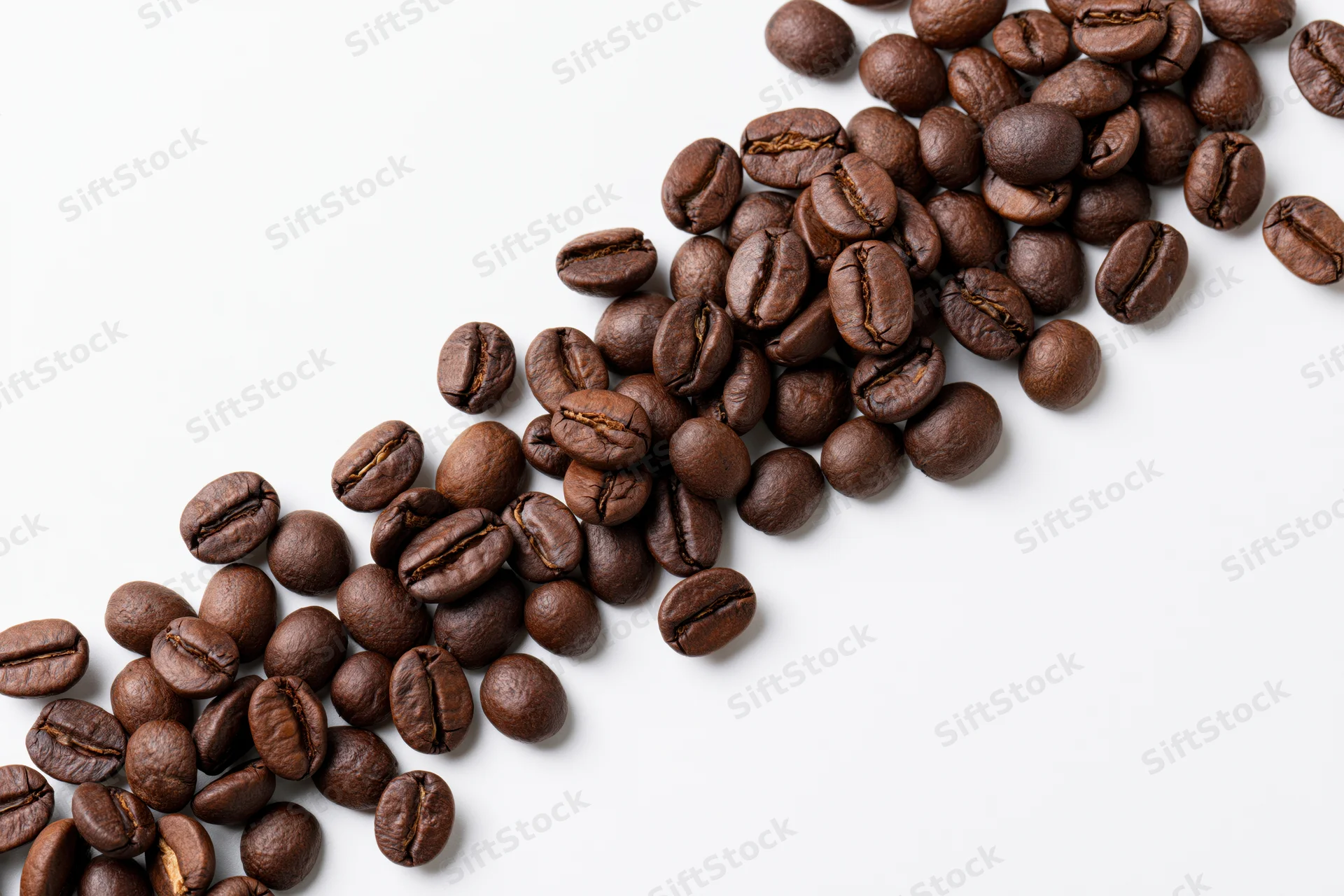 Roasted coffee beans scattered in a loose diagonal cascade on white background