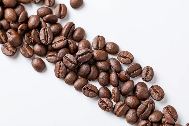 Roasted coffee beans scattered in a loose diagonal cascade on white background
