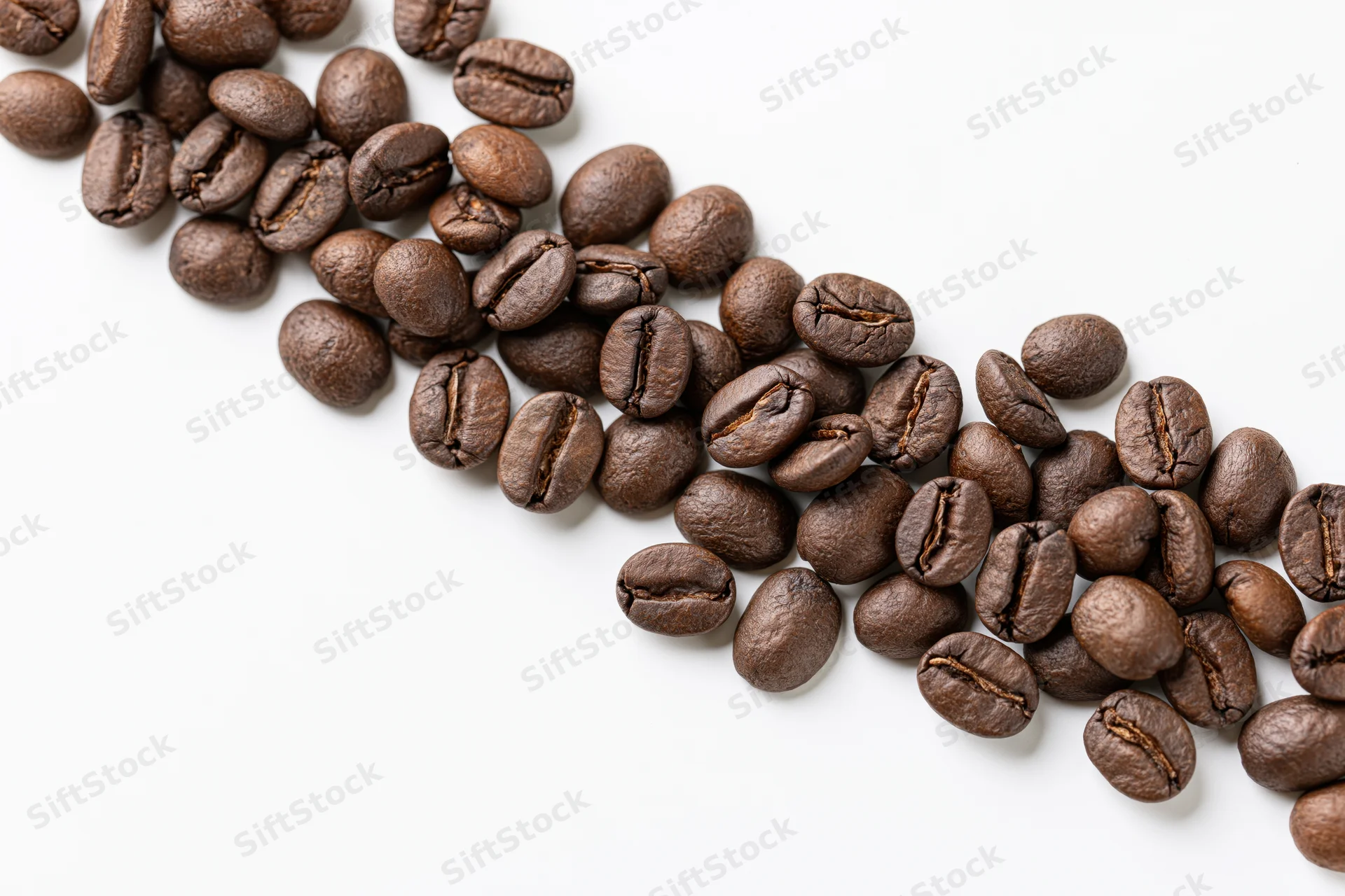 Roasted coffee beans scattered in a loose diagonal cascade on white background