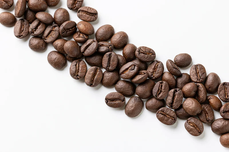 Roasted coffee beans scattered in a loose diagonal cascade on white background