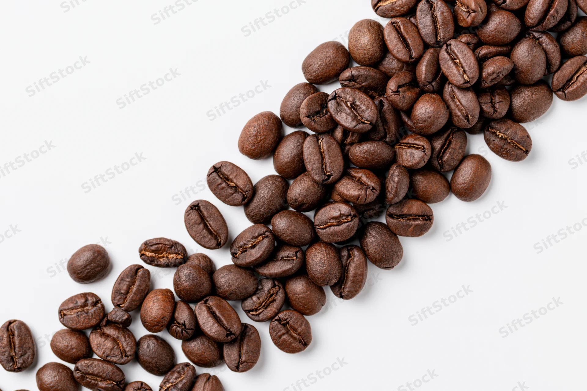 Roasted coffee beans scattered in a loose diagonal cascade on white background