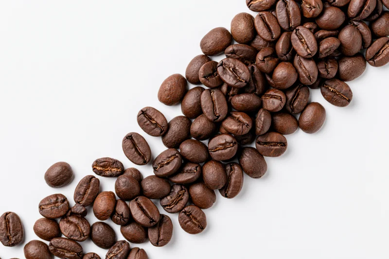 Roasted coffee beans scattered in a loose diagonal cascade on white background