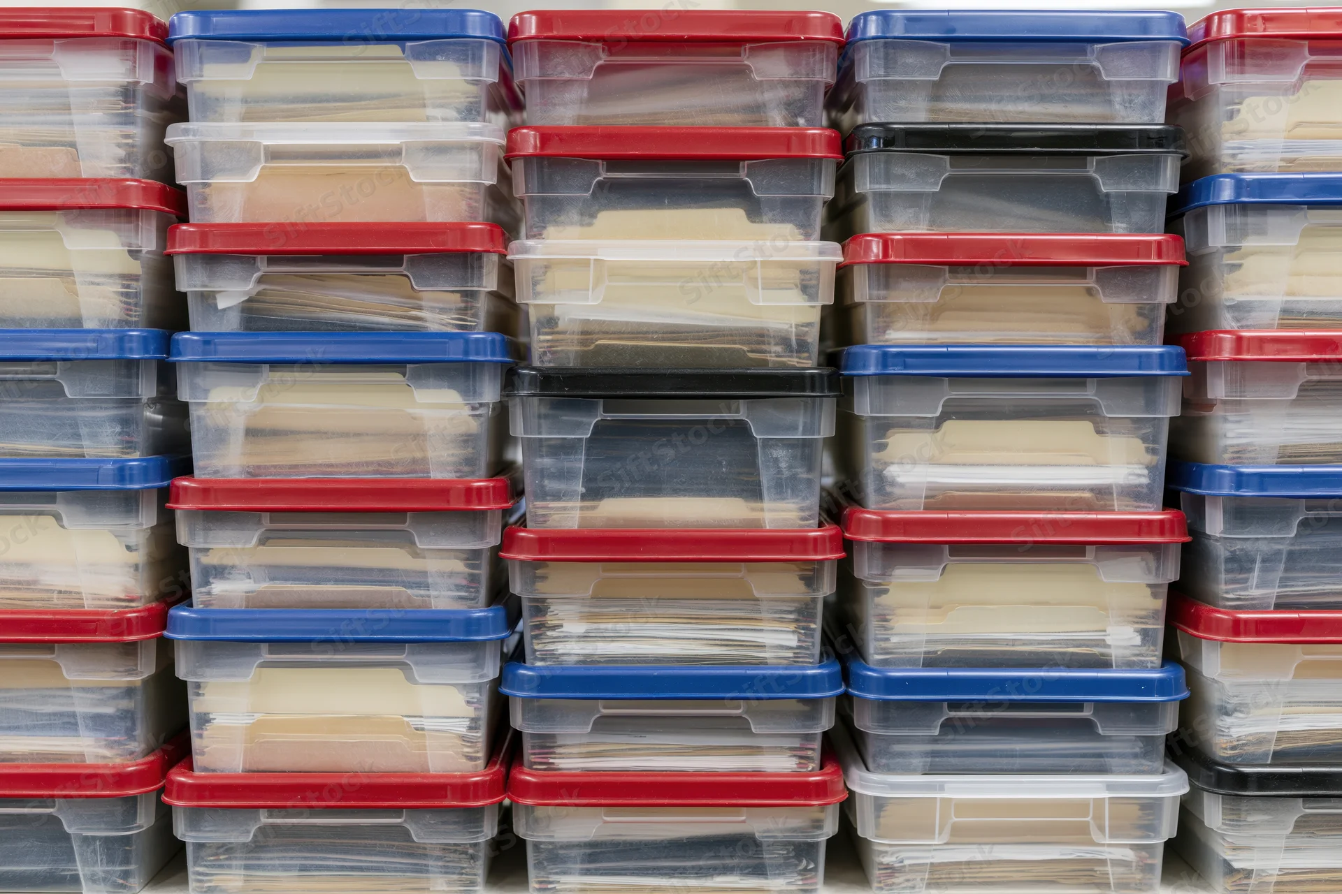 Rows of clear plastic storage bins with red and blue lids stacked on shelves for document organization