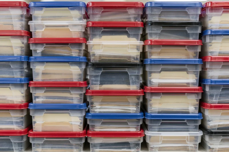 Rows of clear plastic storage bins with red and blue lids stacked on shelves for document organization