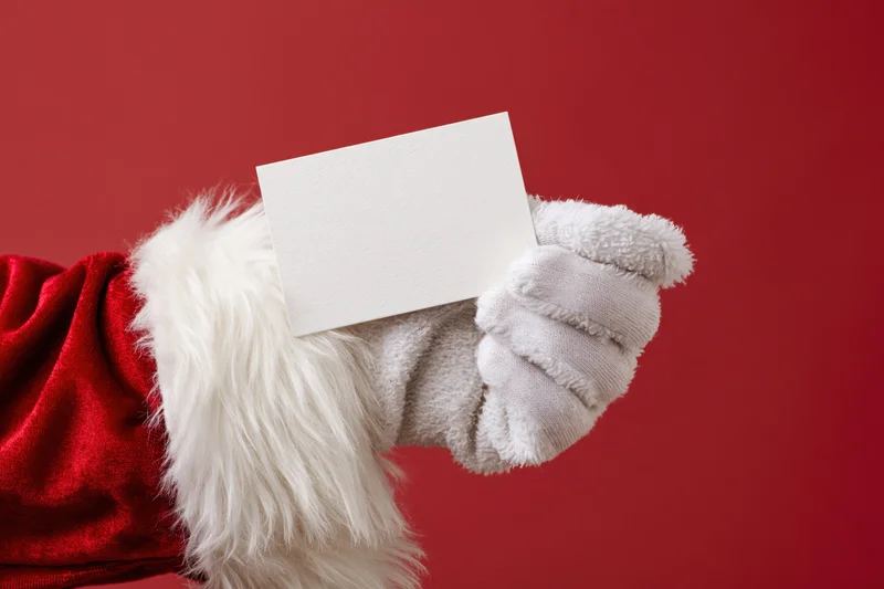 Santa claus gloved hand holding a blank white card against red background