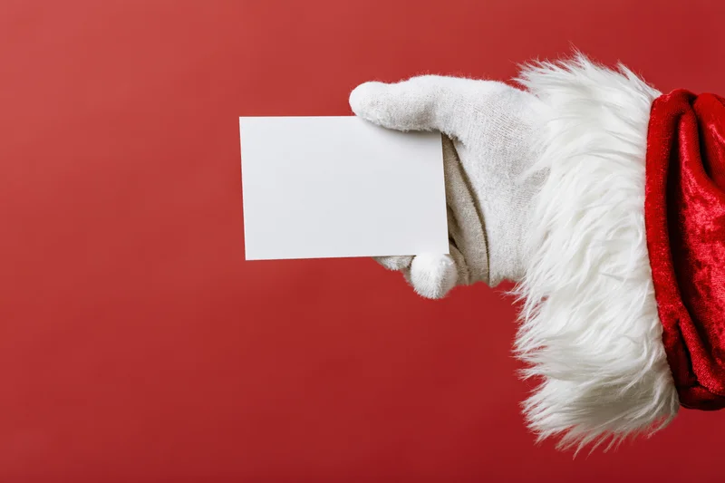 Santa's gloved hand holding a blank white card against red background
