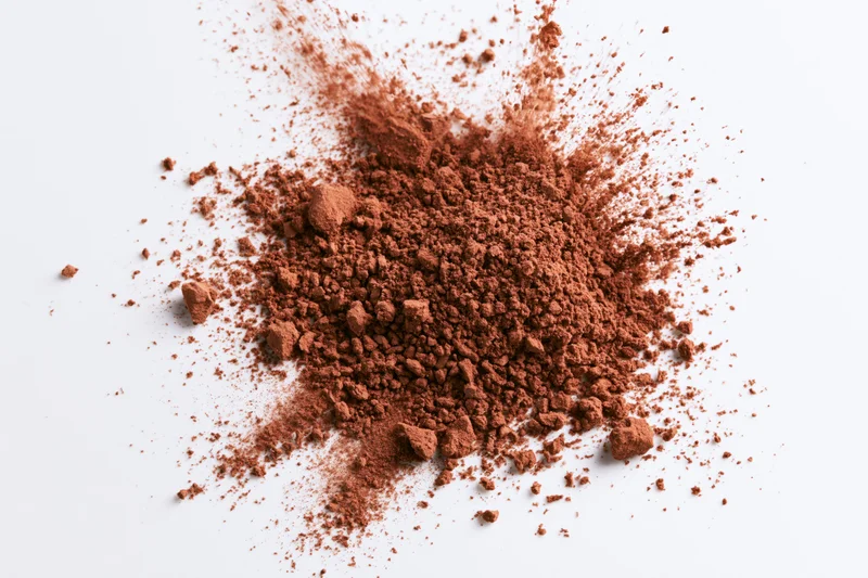 Scattered cocoa powder and coarse brown spice granules on white surface