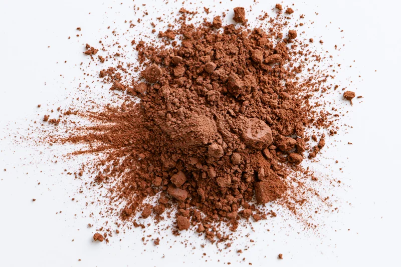 Scattered cocoa powder and brown spice granules on white background