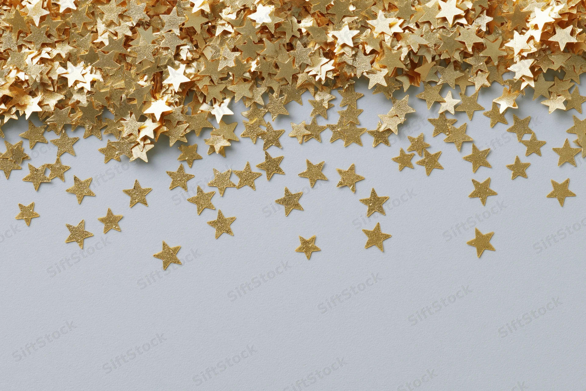 Gold metallic star-shaped confetti scattered in a cluster along the top edge of a light surface, leaving copyspace below