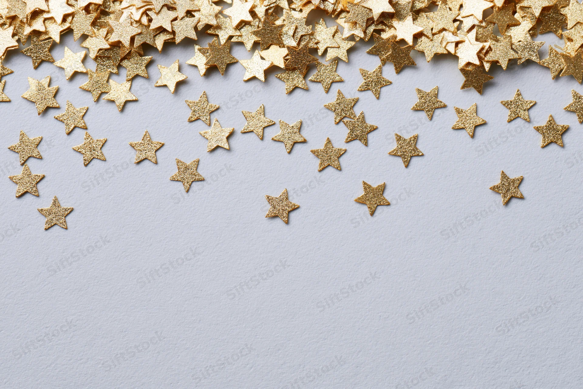 Scattered gold metallic star-shaped confetti pieces on a white surface with copyspace