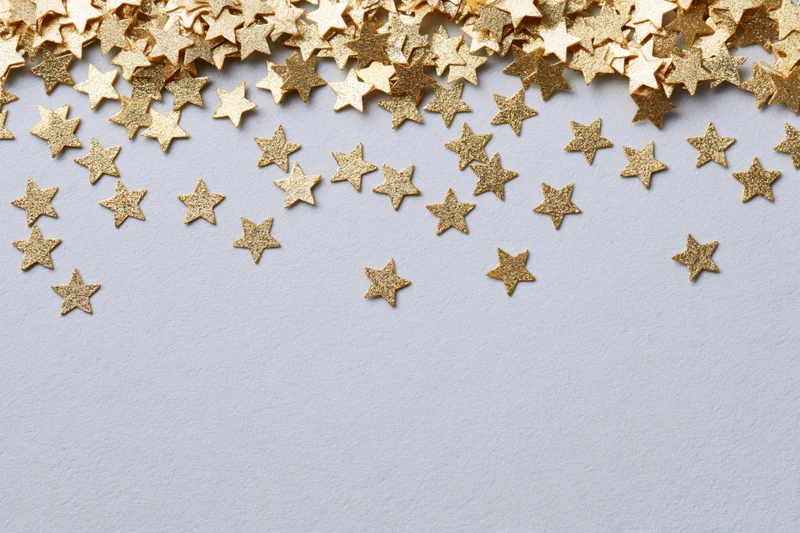 Scattered gold metallic star-shaped confetti pieces on a white surface with copyspace
