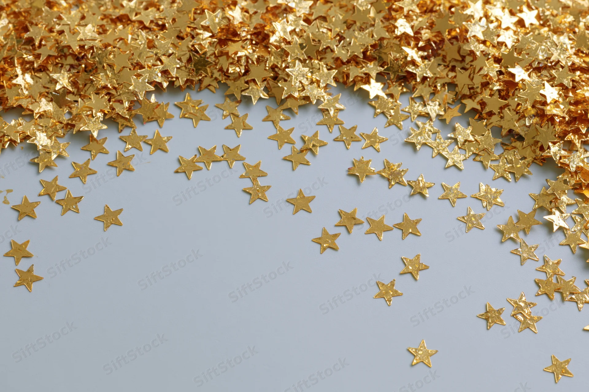 Gold metallic star-shaped confetti scattered across a light blue surface with copyspace