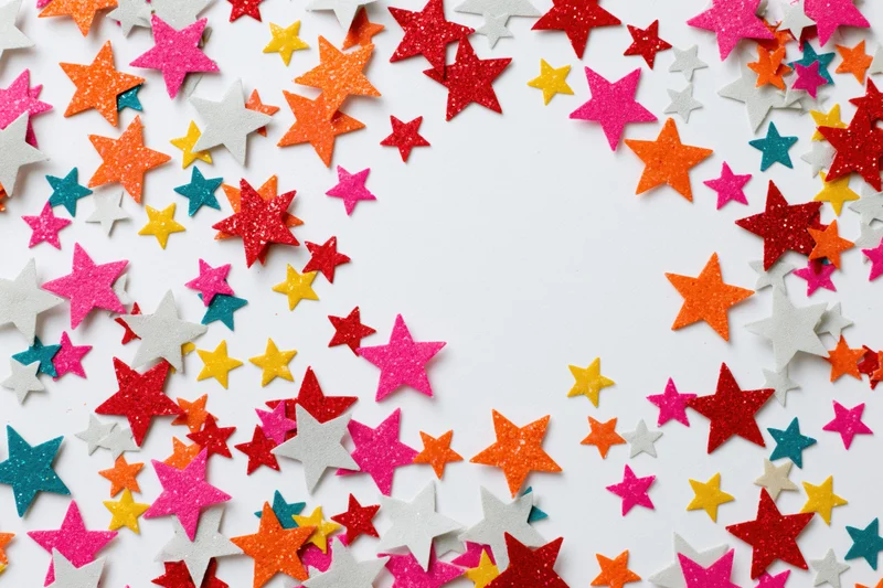Star-shaped confetti pieces scattered across white surface with central copyspace